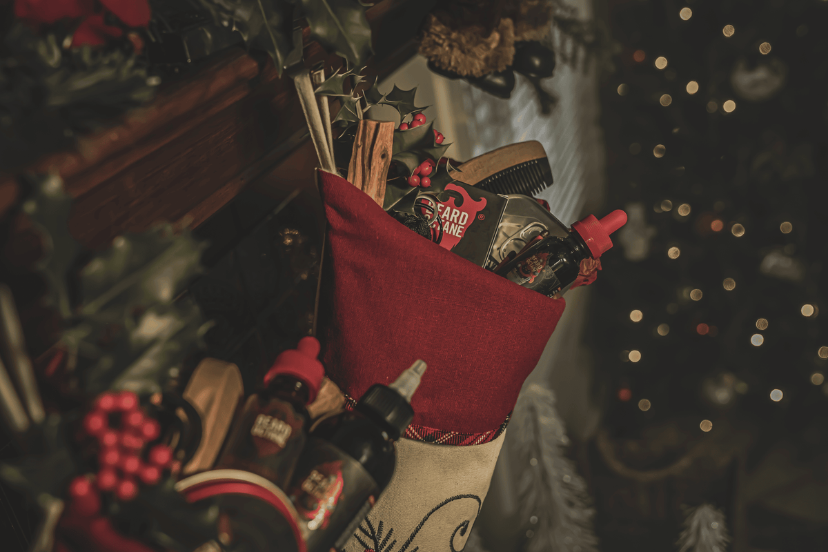 A festive Christmas stocking filled with beard grooming products, including beard oil, combs, and trimmers, surrounded by holiday decorations and blurred Christmas lights in the background.
