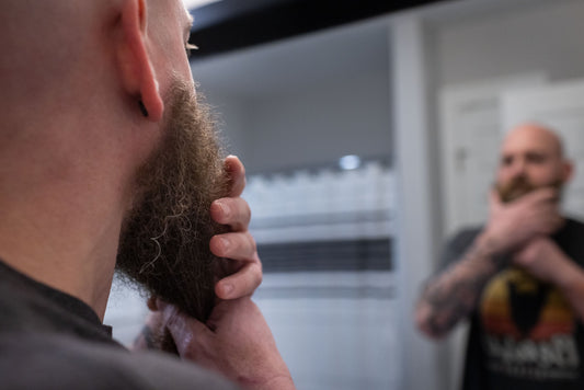 Close-up of a man with a beard, touching his chin in front of a mirror, illustrating beard grooming and care tips for Australian beardsmen.