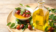 A glass bottle of jojoba oil with fresh jojoba seeds and leaves, highlighting its benefits in beard oil for skin nourishment and hair health.